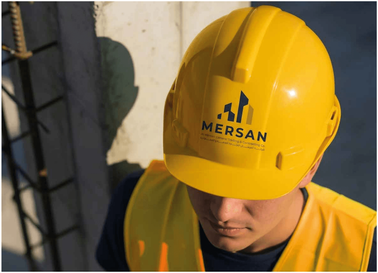 A construction worker wearing an ALMERSAN-branded hard hat and safety vest on a job site